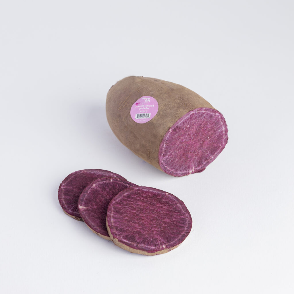 Happy Dirt organic purple sweet potato with slices showing vibrant purple flesh, photographed on a white background.