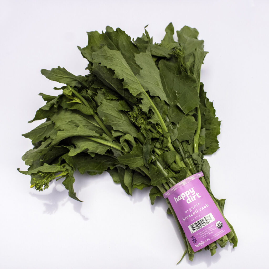 organic broccoli raab with a pink happy dirt skirt tag, laying on a white surface.
