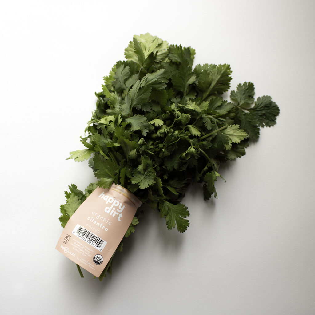 one bunch of organic cilantro with an orange happy dirt skirt tag, laying on a white surface.