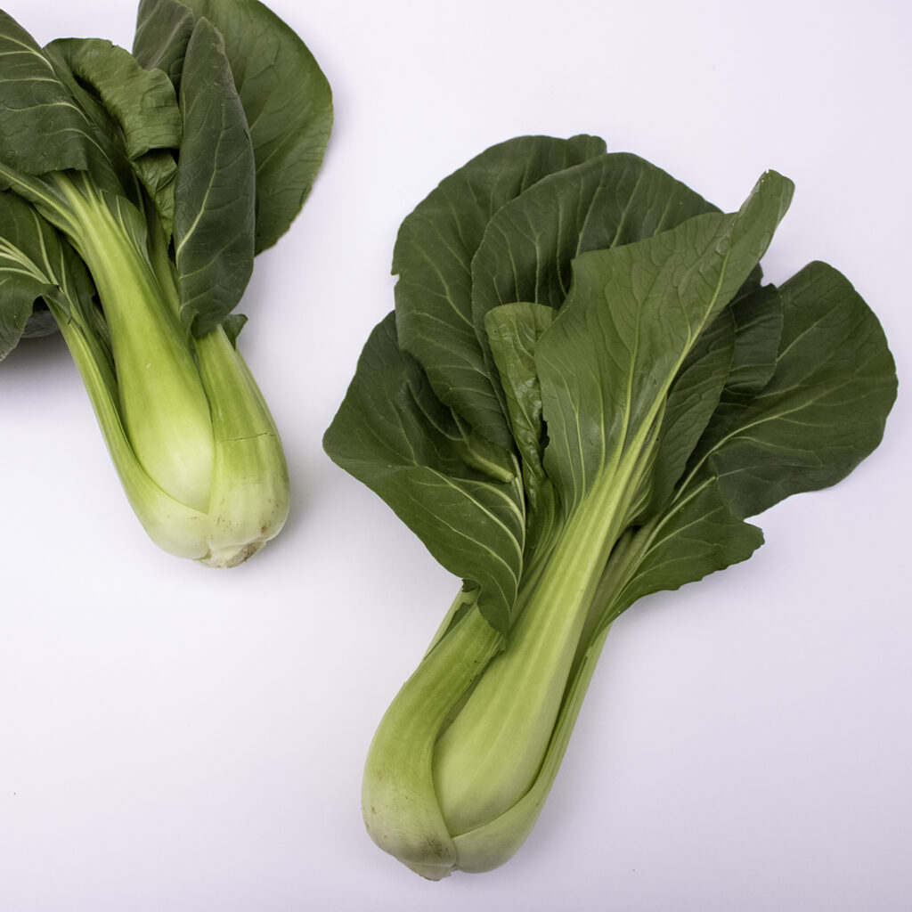 two organic baby bok choy laying on a white surface