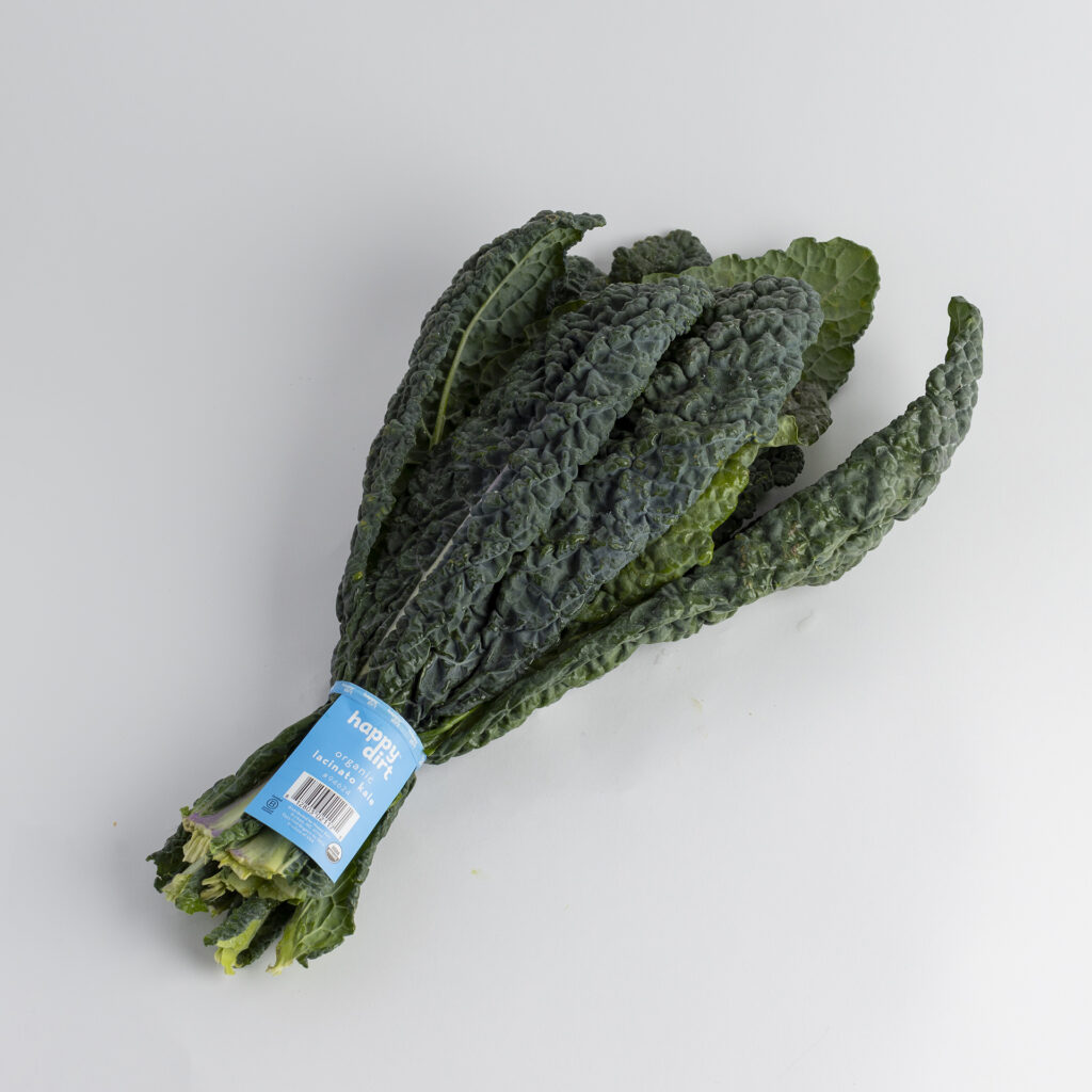 A fresh bunch of Happy Dirt organic Lacinato kale, also known as dinosaur kale, with dark green textured leaves. The bunch is wrapped in a teal Happy Dirt label featuring the USDA Organic seal, barcode, and website, photographed on a clean white background.