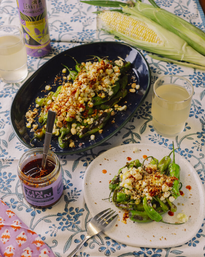Charred organic shishito pepper recipe with corn salad, Tin Man Turkish chili oil, toasted peanuts, and benne seeds served on a platter.